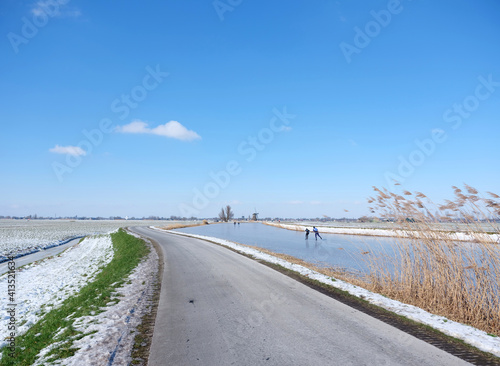 people skate on the ice on canal in alblasserwaard under blue sky