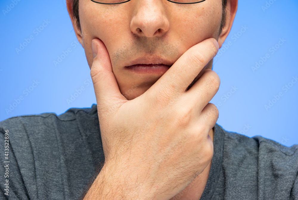 Fototapeta premium Unrecognizable cropped Caucasian male head with hand on face worried pensive gesture isolated on blue studio shot