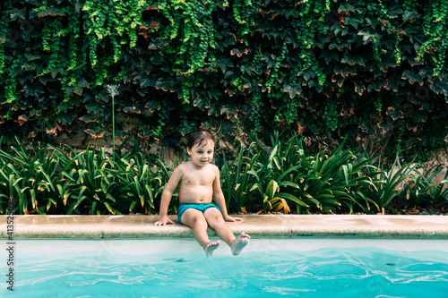 Little boy alone sitting in the border of swimming pool.