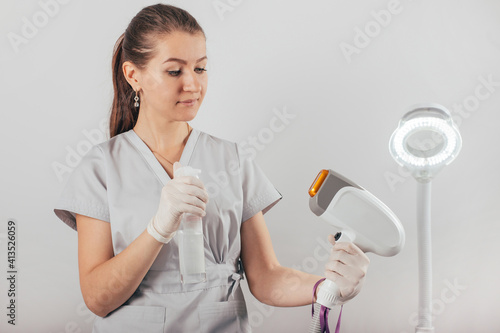 A woman tunes a laser hair removal machine. She holds a working part of the epilator in her hands and poses for a photo. It is located in a modern beauty salon. Body Care. Underarm Laser Hair Removal.