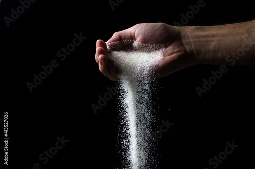 Sugar on a black background. Sugar pours from a man s hand. Excessive sugar intake
