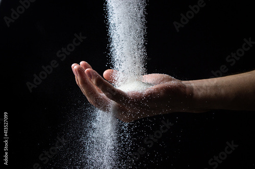 Sugar on a black background. Sugar is poured into a man s hand. Excessive sugar intake