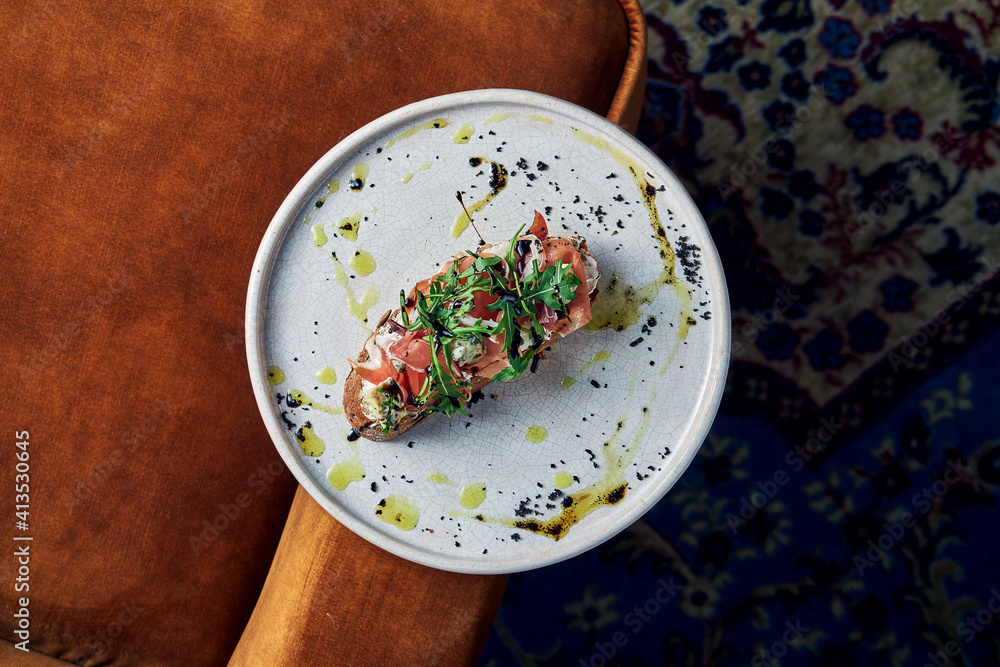Bruschetta with prosciutto, gorgonzola and arugula on rye bread, served in a white plate. Restaurant food. View from above. Italian cuisine Bruschetta with prosciutto, gorgonzola and arugula on rye bread, served in a white plate. Restaurant food. View from above. Italian cuisine