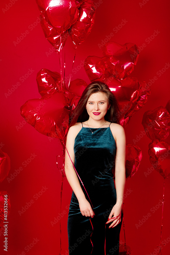 Young woman in long dress with red heart-shaped balloons on red background 