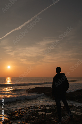 Man looking at the sunset with hand in pocket in the Atlantic ocean in Portugal