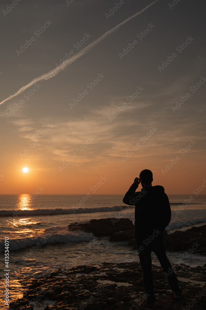 Man watching the sunset putting on his glasses in the Atlantic ocean in Portugal