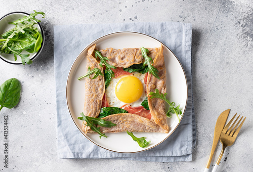 homemade buckwheat crepe galette with egg, ham and spinach on gray background. Traditional French dish. top view photo