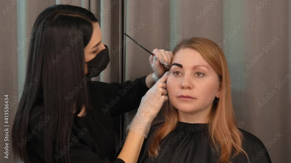 Master apply paint with a brush on brow close up. Professional modern styling, correction, coloring procedures of female eyebrow in beauty salon Master apply paint with a brush on brow close up. Professional modern styling, correction, coloring procedures of female eyebrow in beauty salon