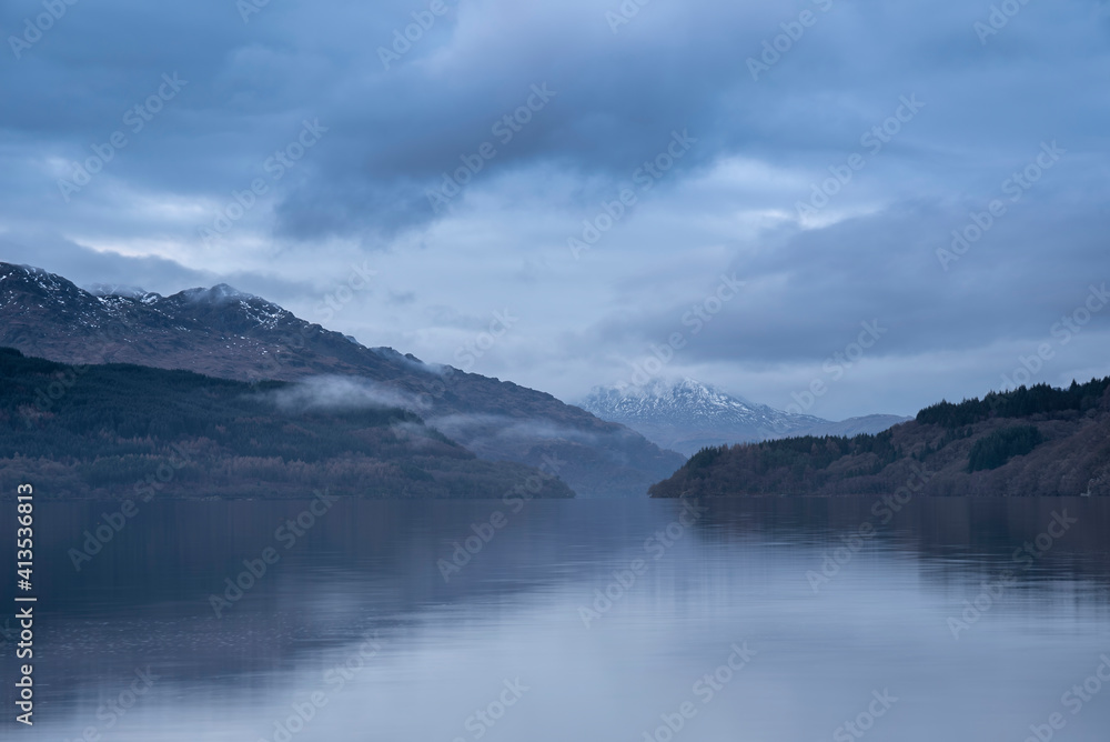 Obraz premium Majestic landscape image across Loch Lomond looking towards snow capped Ben Lui mountain peak in Scottish Highlands