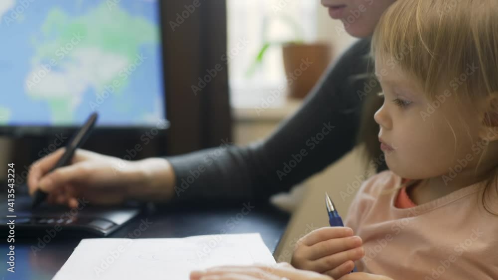 Online working during lockdown with a child, mommy and baby are drawing. Tender woman hand uses tab and a digial pen, kids hands writing on a paper. Cute interested blond girl by the computer table Online working during lockdown with a child, mommy and baby are drawing. Tender woman hand uses tab and a digial pen, kids hands writing on a paper. Cute interested blond girl by the computer table