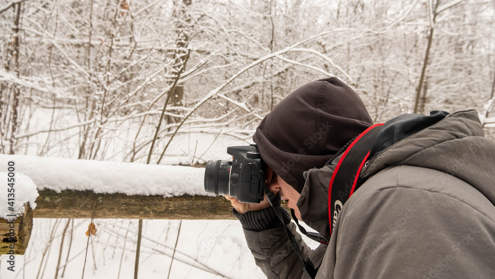 London, Canada, January 19, 2021: Editorial photo of a man in a grey jacket taking pictures outside. Winter day in London, Canada with snow on trees and ground.