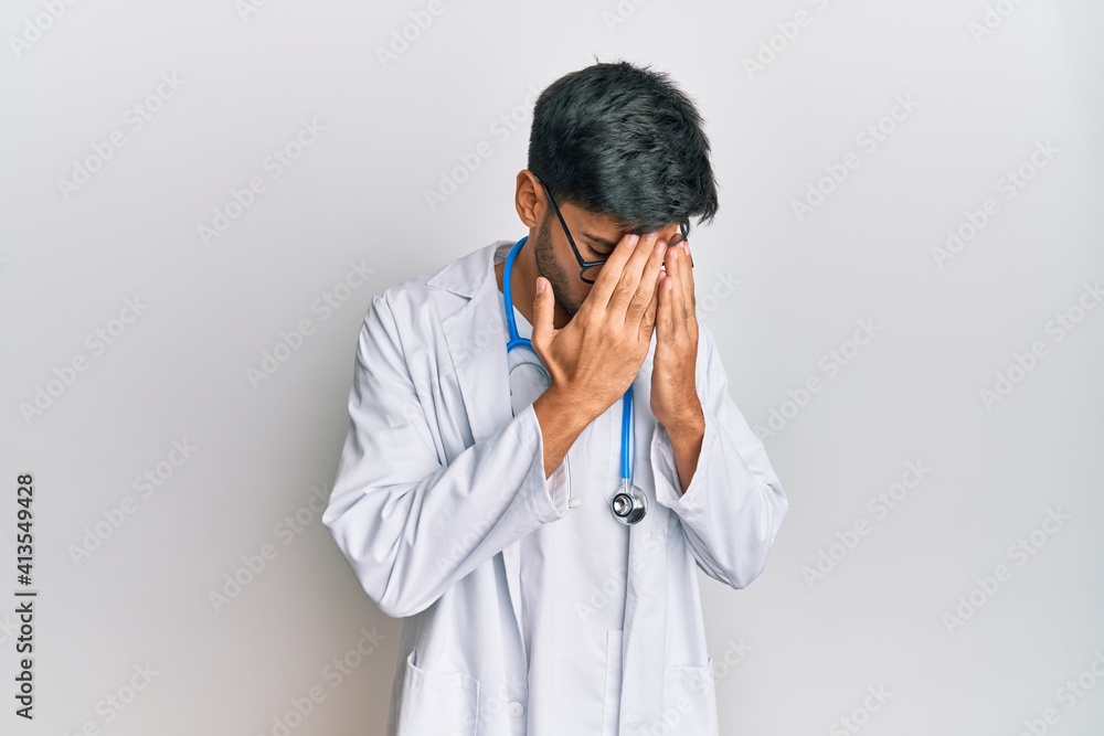Young handsome man wearing doctor uniform and stethoscope with sad expression covering face with hands while crying. depression concept. Young handsome man wearing doctor uniform and stethoscope with sad expression covering face with hands while crying. depression concept.