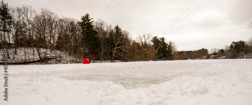 Cleared off ice skating rink on frozen pond in Dorchester, Canada. White snow moved for ice hockey rink on frozen water. Red ice fishing tent on frozen lake