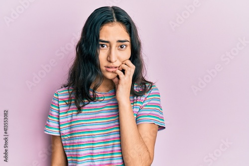 Hispanic teenager girl with dental braces wearing casual clothes looking stressed and nervous with hands on mouth biting nails. anxiety problem.