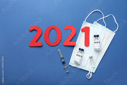 Flat lay composition with coronavirus vaccine and number 2021 on blue background photo