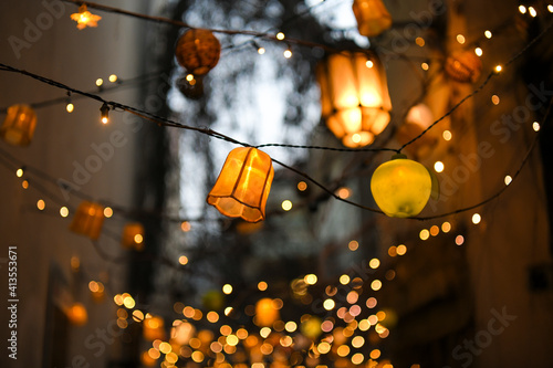Colorful lampions and lanterns up a tree at night in the garden. A wedding, event or festival banquet decoration at night. Garlands of lamps on a tree branches. Row of paper lampions.