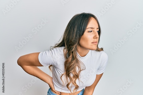 Young brunette woman wearing casual white t shirt suffering of backache, touching back with hand, muscular pain