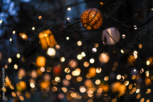 Colorful lampions and lanterns up a tree at night in the garden. A wedding, event or festival banquet decoration at night. Garlands of lamps on a tree branches. Row of paper lampions.