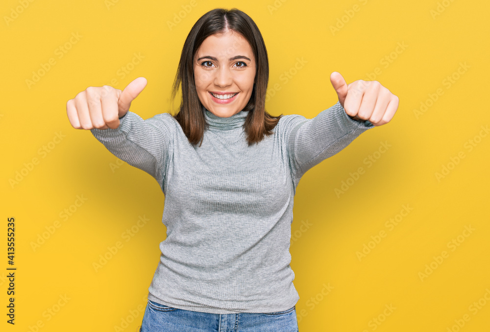 Young beautiful woman wearing casual turtleneck sweater approving doing positive gesture with hand, thumbs up smiling and happy for success. winner gesture. Young beautiful woman wearing casual turtleneck sweater approving doing positive gesture with hand, thumbs up smiling and happy for success. winner gesture.