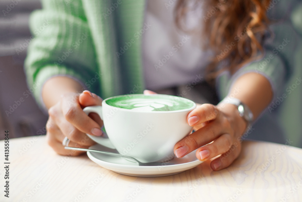 Unfocused woman hands holding cup of hot butterfly pea latte or blue spirulina latte on wooden table Unfocused woman hands holding cup of hot butterfly pea latte or blue spirulina latte on wooden table