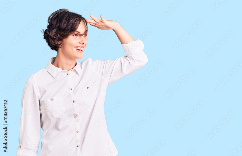Beautiful young woman with short hair wearing elegant white shirt very happy and smiling looking far away with hand over head. searching concept. Beautiful young woman with short hair wearing elegant white shirt very happy and smiling looking far away with hand over head. searching concept.
