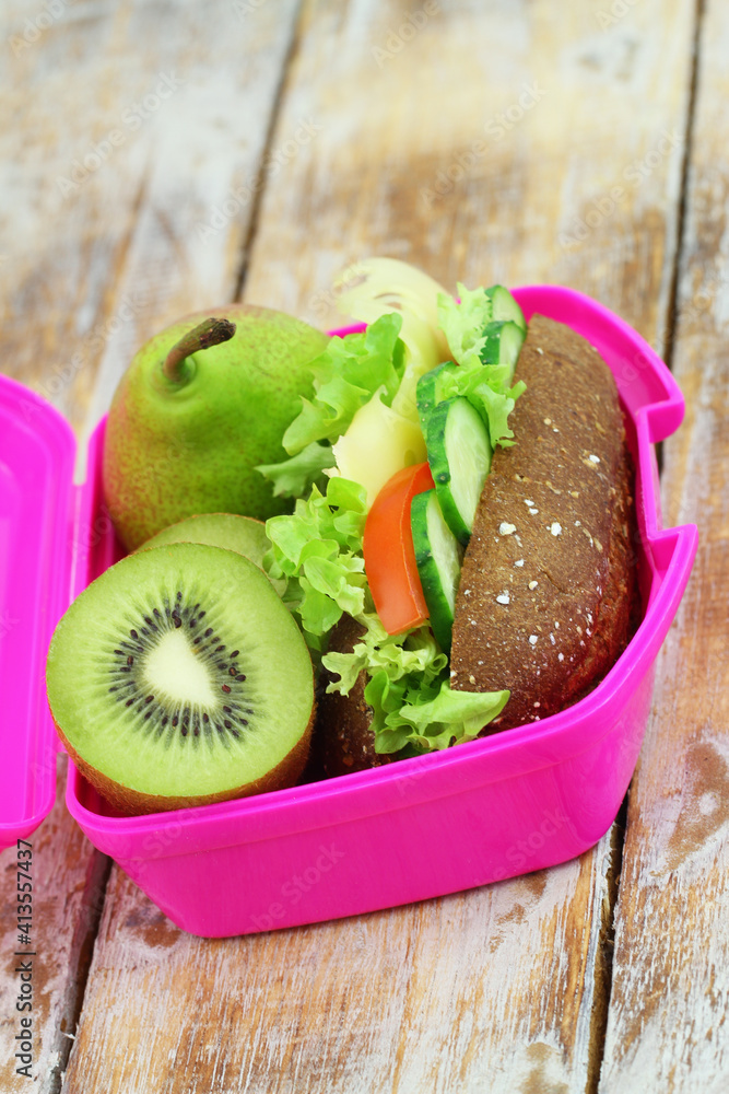 Healthy lunch box with whole grain roll with Swiss cheese, lettuce, tomato and cucumber and kiwi fruit