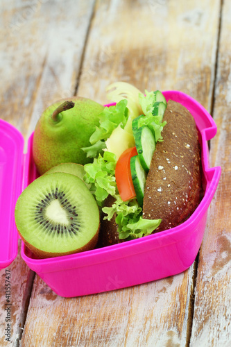 Obraz na płótnie Healthy lunch box with whole grain roll with Swiss cheese, lettuce, tomato and cucumber and kiwi fruit
w salonie