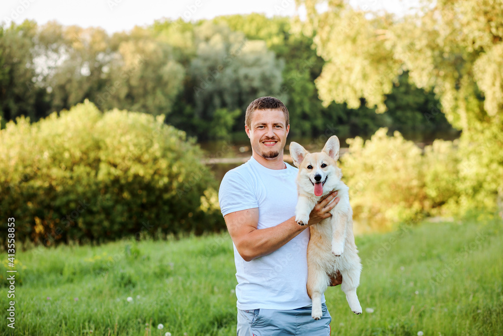 Handsome young man is holding Welsh Corgi Pembroke dog. Green park background. Handsome young man is holding Welsh Corgi Pembroke dog. Green park background.