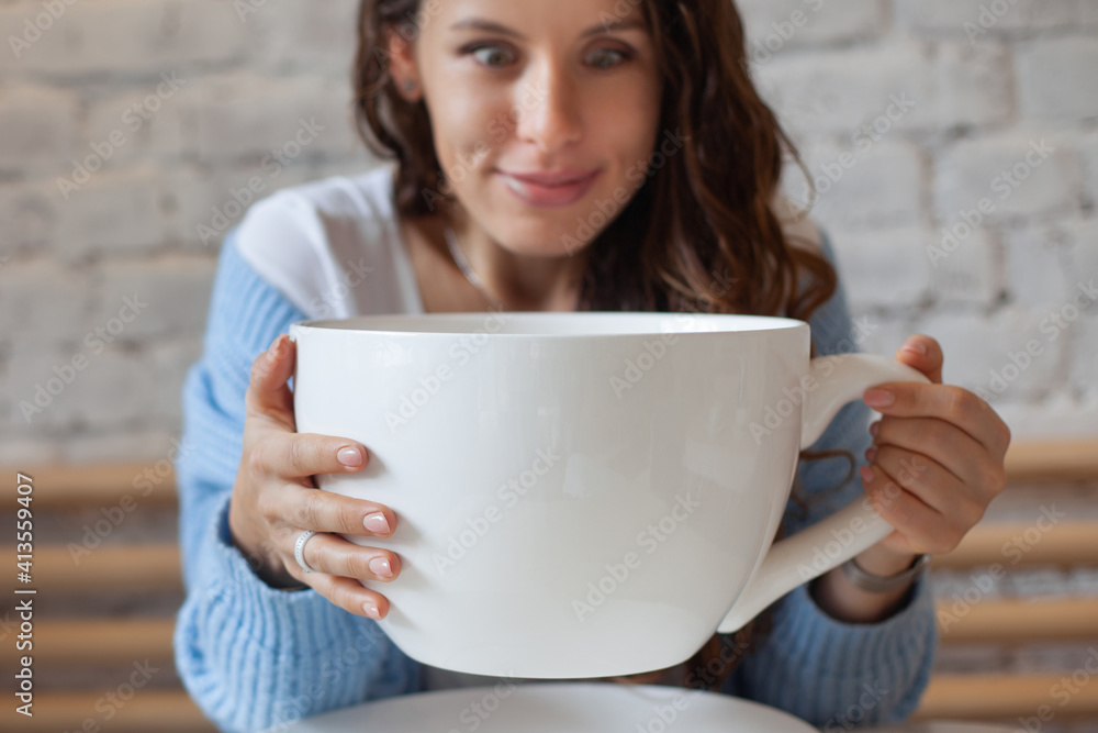 Young woman in blue sweater is feeling headache, with head in hand and holding big cup hot drink. Young woman in blue sweater is feeling headache, with head in hand and holding big cup hot drink.
