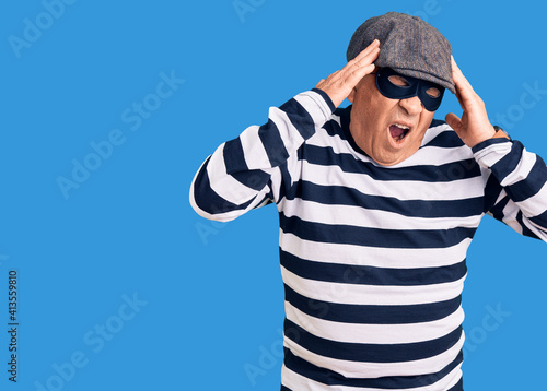 Senior handsome man wearing burglar mask and t-shirt with hand on head, headache because stress. suffering migraine.