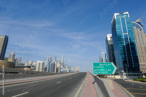 Vue sur une route surélevée traversant un quartier d'affaires au centre ville de Dubaï. Un panneau indicateur routier vert au premier plan.