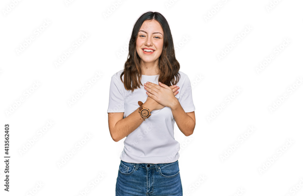 Young beautiful woman wearing casual white t shirt smiling with hands on chest with closed eyes and grateful gesture on face. health concept. Young beautiful woman wearing casual white t shirt smiling with hands on chest with closed eyes and grateful gesture on face. health concept.