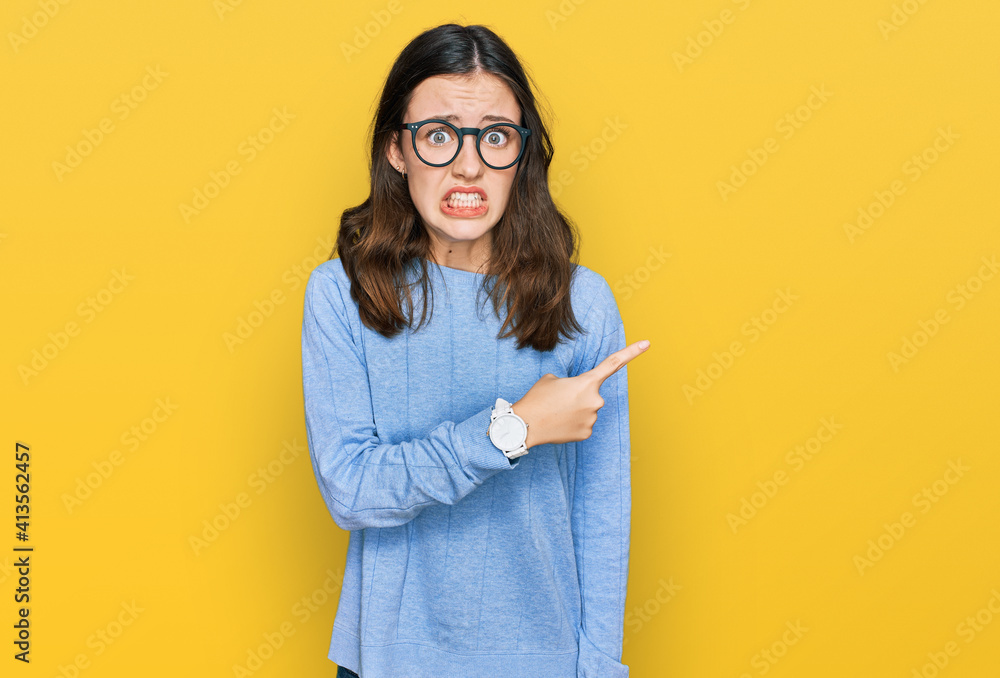 Young beautiful woman wearing casual clothes and glasses pointing aside worried and nervous with forefinger, concerned and surprised expression Young beautiful woman wearing casual clothes and glasses pointing aside worried and nervous with forefinger, concerned and surprised expression