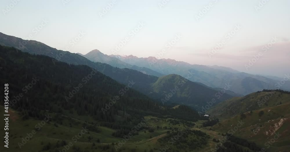 Dawn in the green mountains. High hills covered with grass and forest. Coniferous trees cast shadows from the sun. Trails and tents are visible. View from the drone from above. Kok Zhailau Mountains. Dawn in the green mountains. High hills covered with grass and forest. Coniferous trees cast shadows from the sun. Trails and tents are visible. View from the drone from above. Kok Zhailau Mountains.