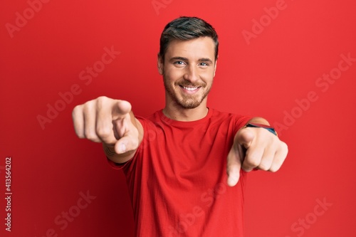 Handsome caucasian man wearing casual red tshirt pointing to you and the camera with fingers, smiling positive and cheerful © Krakenimages.com