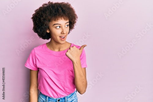 Young hispanic girl wearing casual clothes pointing thumb up to the side smiling happy with open mouth