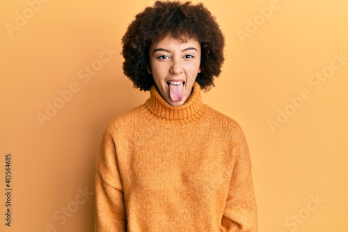 Young hispanic girl wearing wool winter sweater sticking tongue out happy with funny expression. emotion concept. © Krakenimages.com