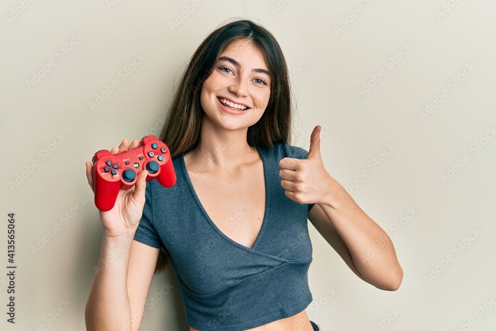 Young caucasian woman playing video game holding controller smiling happy and positive, thumb up doing excellent and approval sign Young caucasian woman playing video game holding controller smiling happy and positive, thumb up doing excellent and approval sign