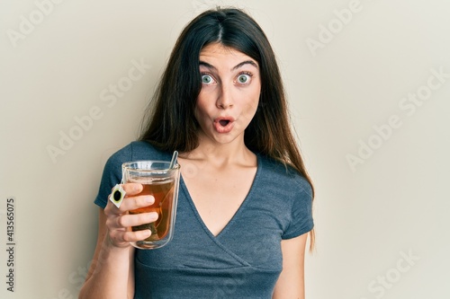 Young caucasian woman holding cup of tea scared and amazed with open mouth for surprise, disbelief face photo