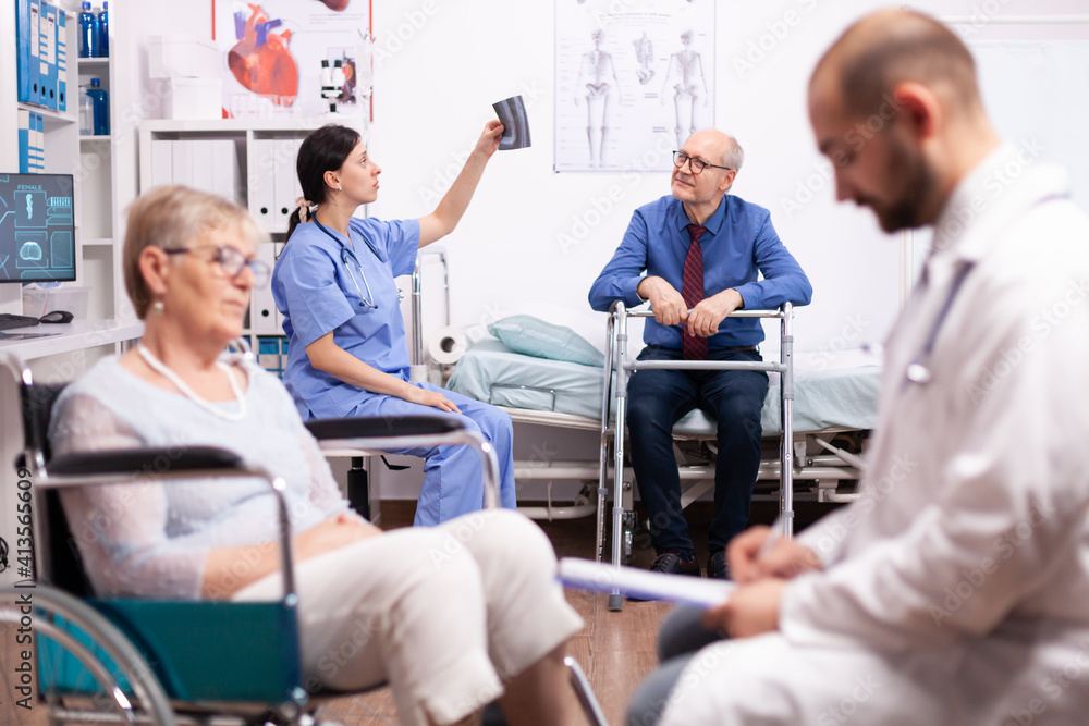 Nurse looking at radiography of handicapped patient sitting on wheelchair. Man with disabilities ,walking frame sitting in hospital bed. Health care system, clinic patients. Nurse looking at radiography of handicapped patient sitting on wheelchair. Man with disabilities ,walking frame sitting in hospital bed. Health care system, clinic patients.