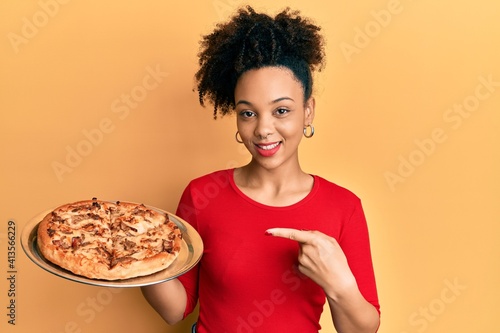 Young african american girl holding italian pizza smiling happy pointing with hand and finger