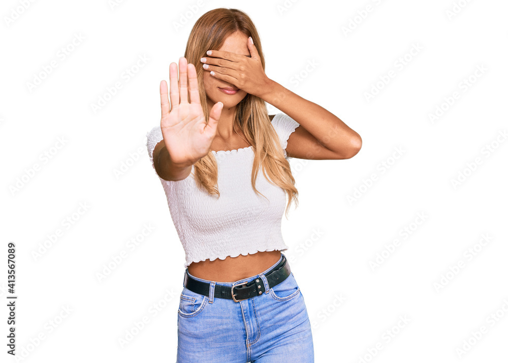 Beautiful blonde young woman wearing casual white tshirt covering eyes with hands and doing stop gesture with sad and fear expression. embarrassed and negative concept. Beautiful blonde young woman wearing casual white tshirt covering eyes with hands and doing stop gesture with sad and fear expression. embarrassed and negative concept.