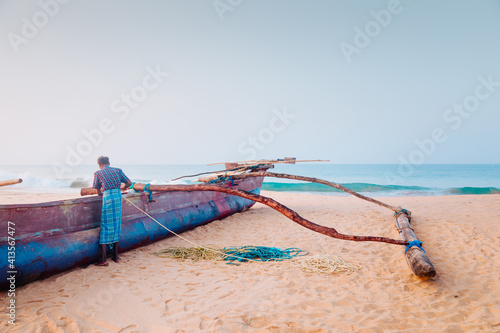 Fototapeta Naklejka Na Ścianę i Meble -  Beautiful morning beach scene. A fisherman, preparing a fishing net, standing near the fishing boat at the ocean sandy coast at Sri-Lanka island.