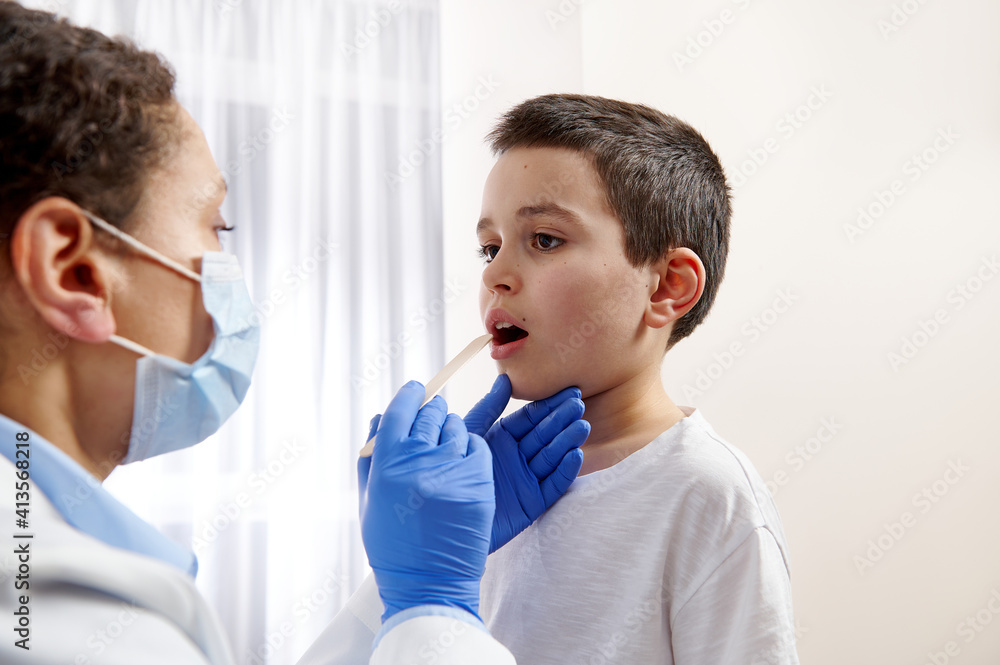 Fototapeta premium Young pediatrician examining little boys throat to diagnose his illness.