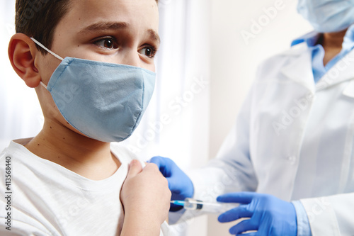 фотографія Terrified boy vaccinated on background of blurred doctor in gloves and white med