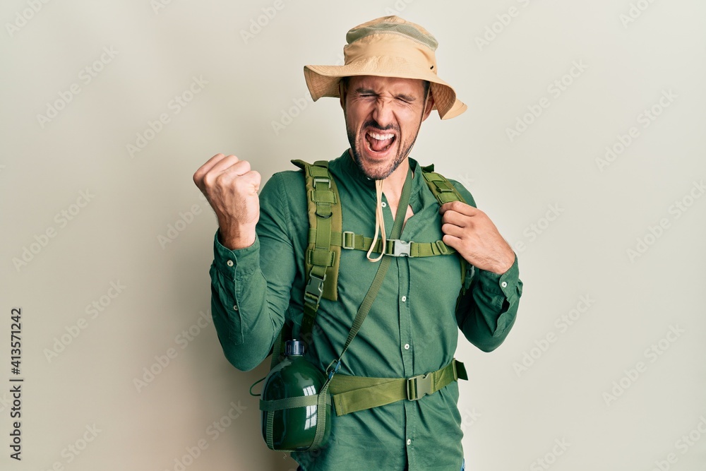 Handsome man with beard wearing explorer hat and backpack very happy and excited doing winner gesture with arms raised, smiling and screaming for success. celebration concept. Handsome man with beard wearing explorer hat and backpack very happy and excited doing winner gesture with arms raised, smiling and screaming for success. celebration concept.
