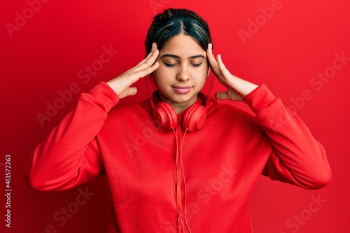 Young latin woman listening to music using headphones with hand on head, headache because stress. suffering migraine. © Krakenimages.com
