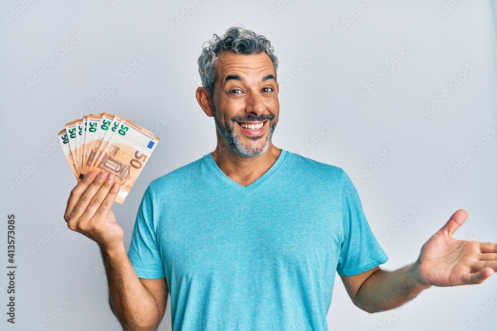 Middle age grey-haired man holding 50 euro banknotes celebrating achievement with happy smile and winner expression with raised hand Middle age grey-haired man holding 50 euro banknotes celebrating achievement with happy smile and winner expression with raised hand