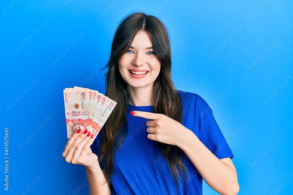 Young beautiful caucasian girl holding 10 colombian pesos banknotes smiling happy pointing with hand and finger Young beautiful caucasian girl holding 10 colombian pesos banknotes smiling happy pointing with hand and finger