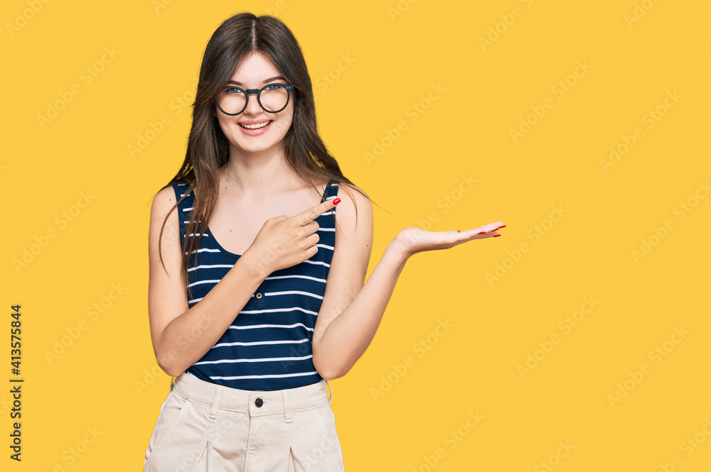 Young beautiful caucasian girl wearing casual clothes and glasses amazed and smiling to the camera while presenting with hand and pointing with finger. Young beautiful caucasian girl wearing casual clothes and glasses amazed and smiling to the camera while presenting with hand and pointing with finger.